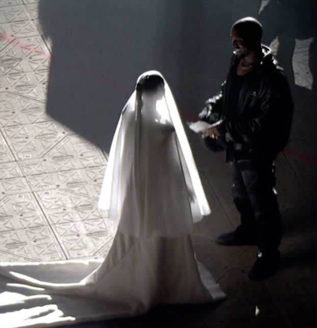Mujer con vestido blanco, parada frente a Kanye West en el Listening Party de DONDA